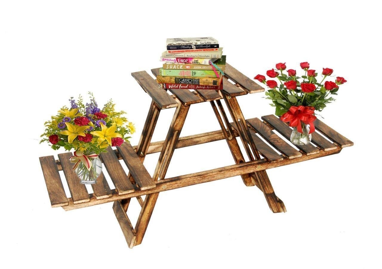 A table with three platforms similar to a picnic table, with flower vases on two ends and books piled on the main table.