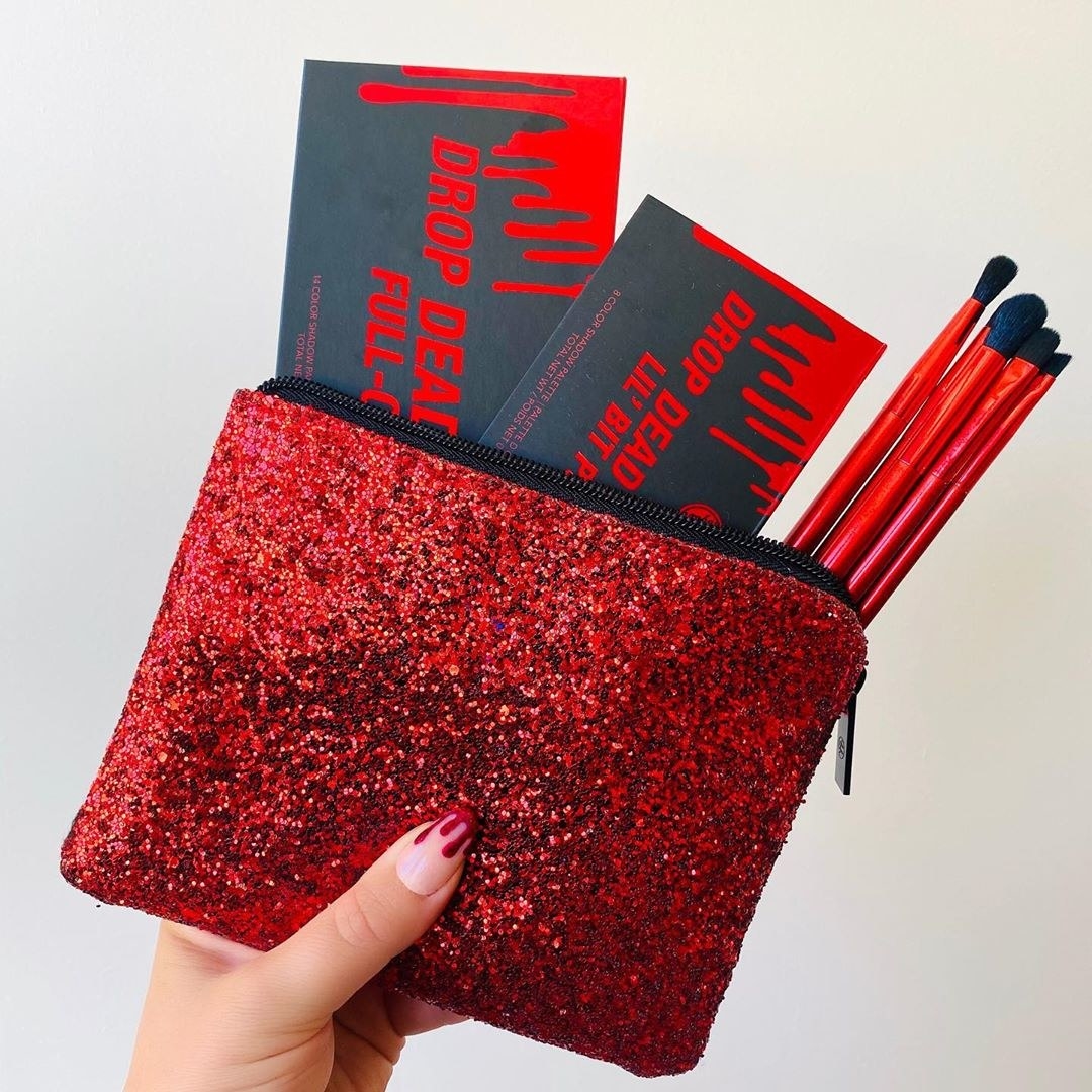 A hand holding the red glitter makeup bag full of the collection&#x27;s products 