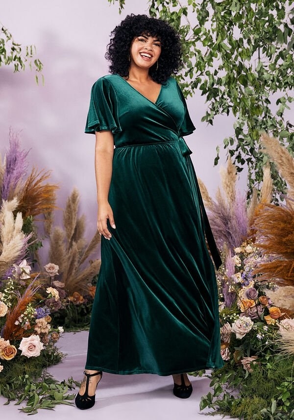 A model in the emerald short-sleeve dress with a tie waist and surplice neckline