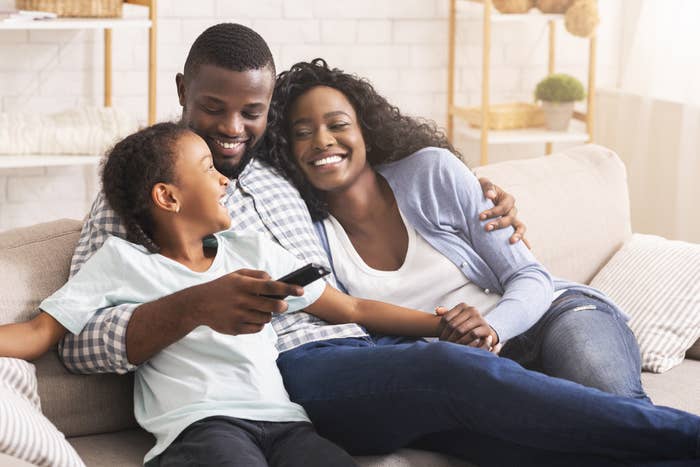 A young boy sits on the sofa with his smiling parents.