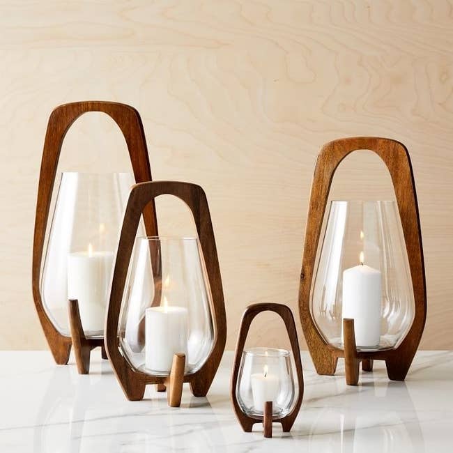 Four candles of different sizes in glass containers balanced on mid-century modern wooden frame 