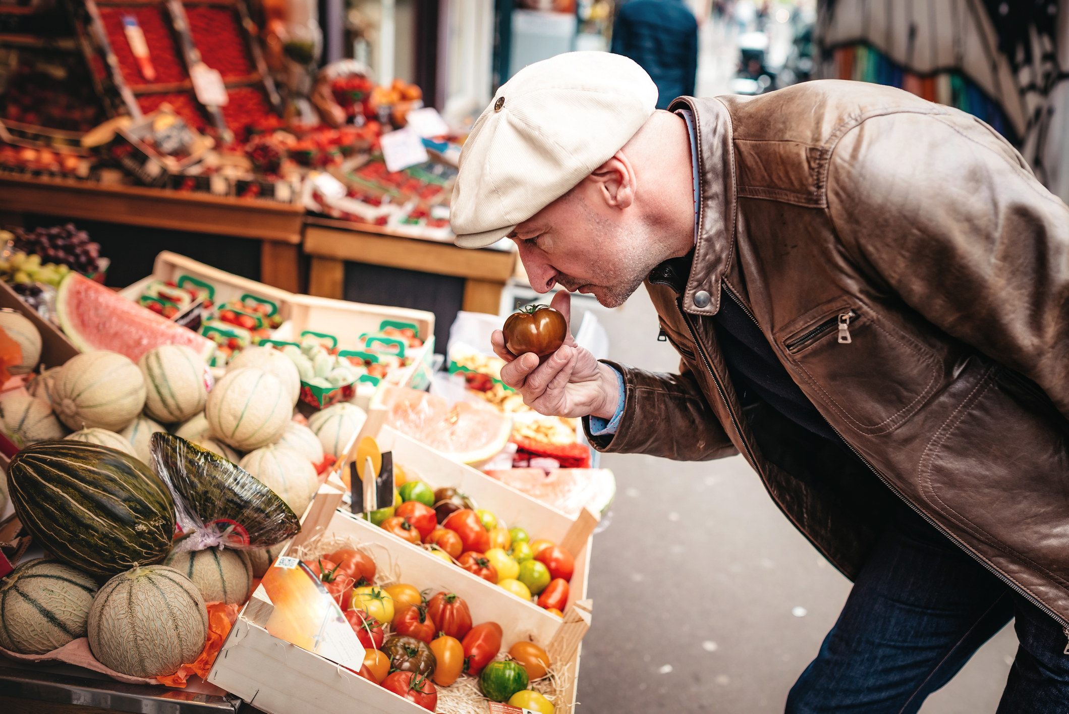 Person smelling a tomato at a veggie stand.