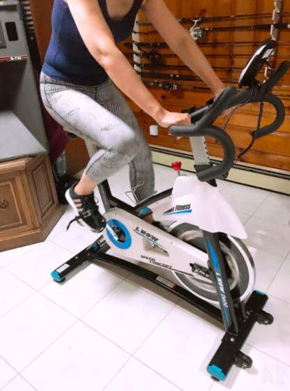 Reviewer cycles on blue, white, and black indoor exercising bike in their home