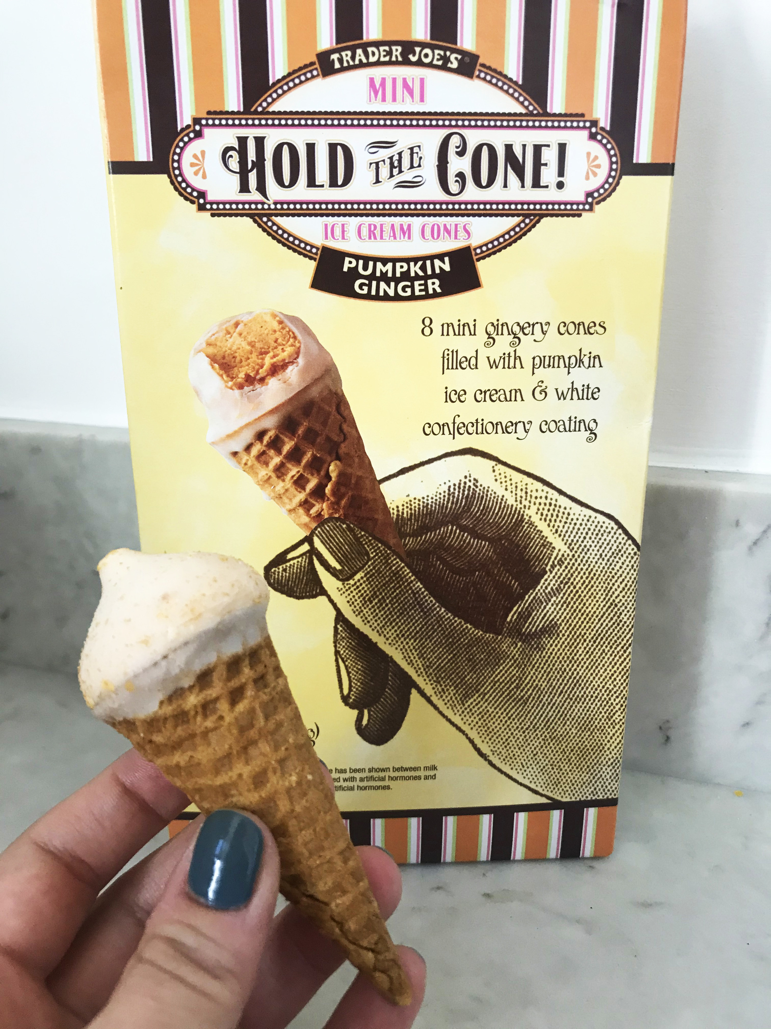 A hand holds up a mini ice cream cone in front of the trader joe&#x27;s hold the cone package