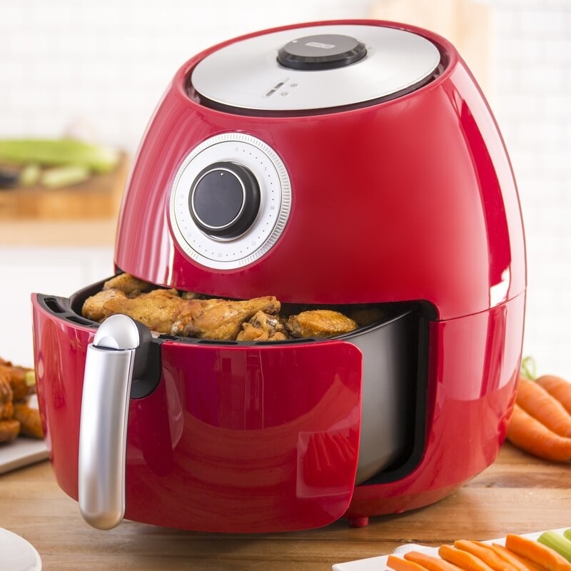 The air fryer in red with chicken wings in the basket