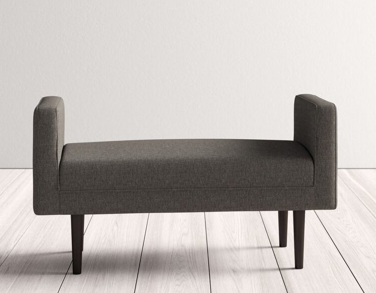 The upholstered bench in grey with dark brown legs and taller arms on each side