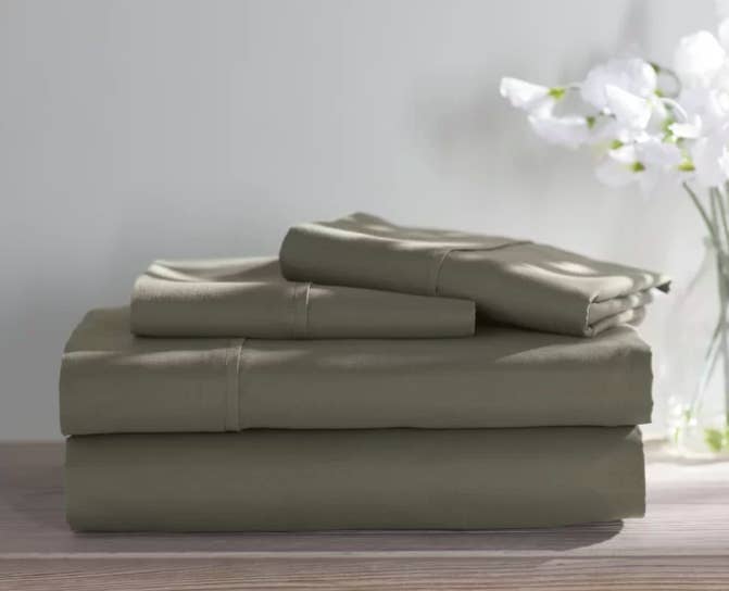 Sage green sheet set folded on a wooden shelf next to a vase with flowers