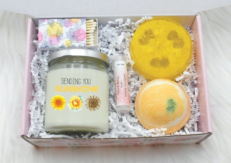 The open box containing the candle, bath bomb, loofah soap, lip balm, and matches
