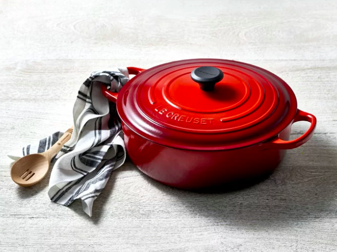 A red Le Creuset Cast Iron Round Dutch Oven next to a striped towel and a wooden spoon