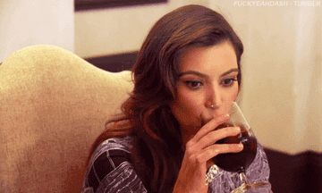 Kim Kardashian raising her eyebrows as she drinks a glass of red wine.
