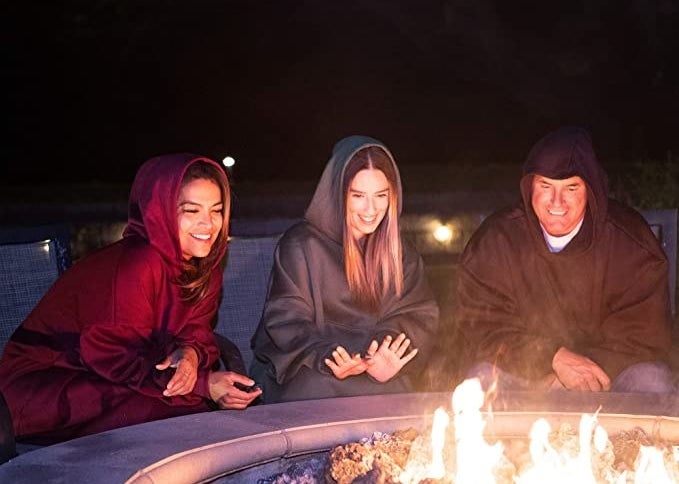 People wear oversized sweaters around a firepit