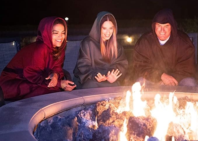 People wear oversized sweaters around a firepit