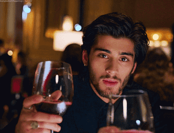 Zayn Malik clinking a glass of wine in a music video.