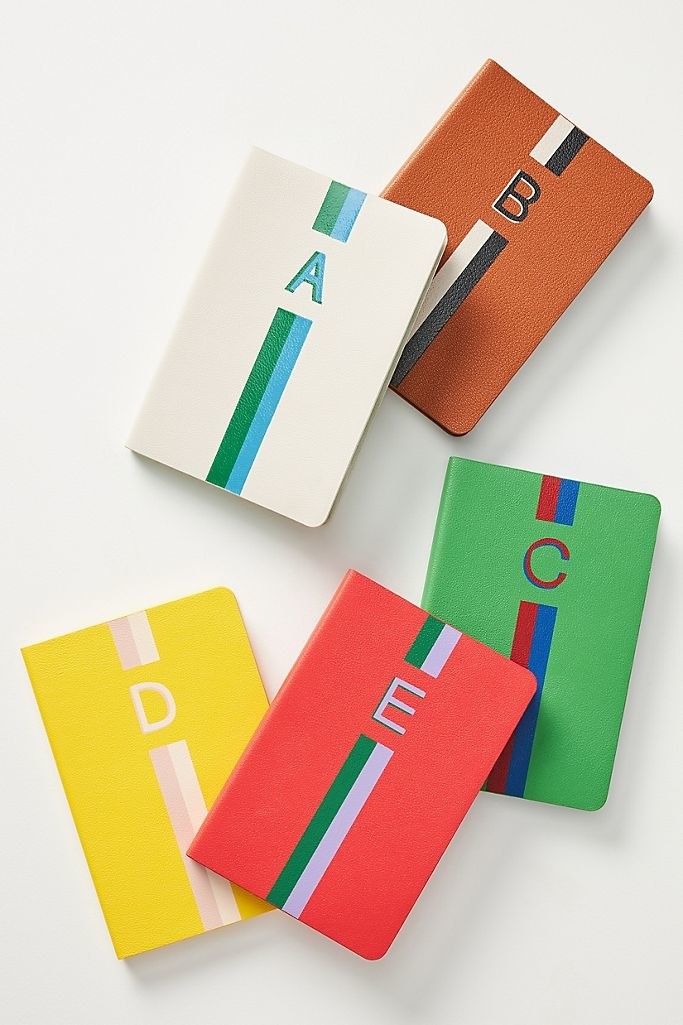 Brightly colored journals with a vibrant striped design, each personalized with a letter on the cover