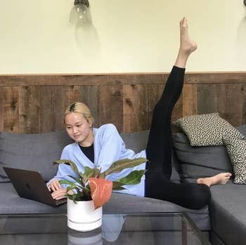 BuzzFeed editor Melanie Aman wearing the ankle-length version of the black leggings while lying on the couch and working on her computer