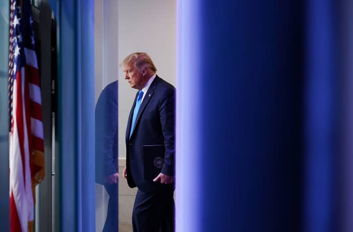 President Donald Trump stands behind a blue curtain and US flag
