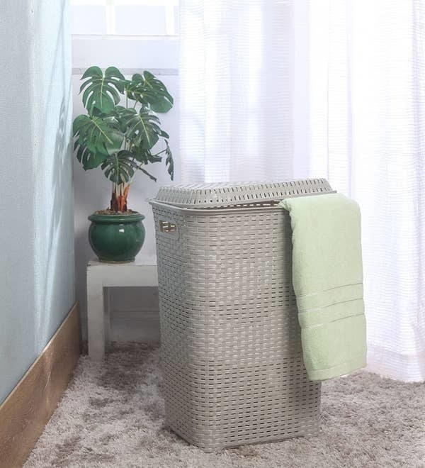 A grey laundry basket with a towel hanging half out of it
