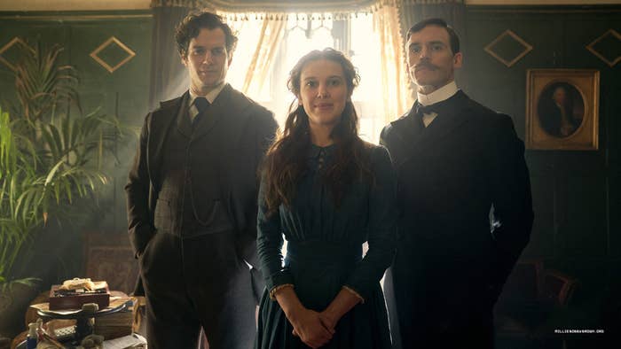 Enola Brown standing between her brothers, Sherlock (left) and Mycroft (right).