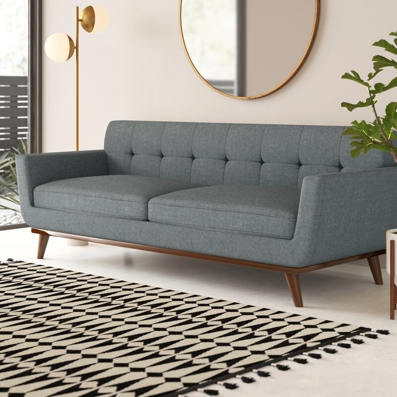 Grey couch with two cushions and a tufted back with brown wood legs