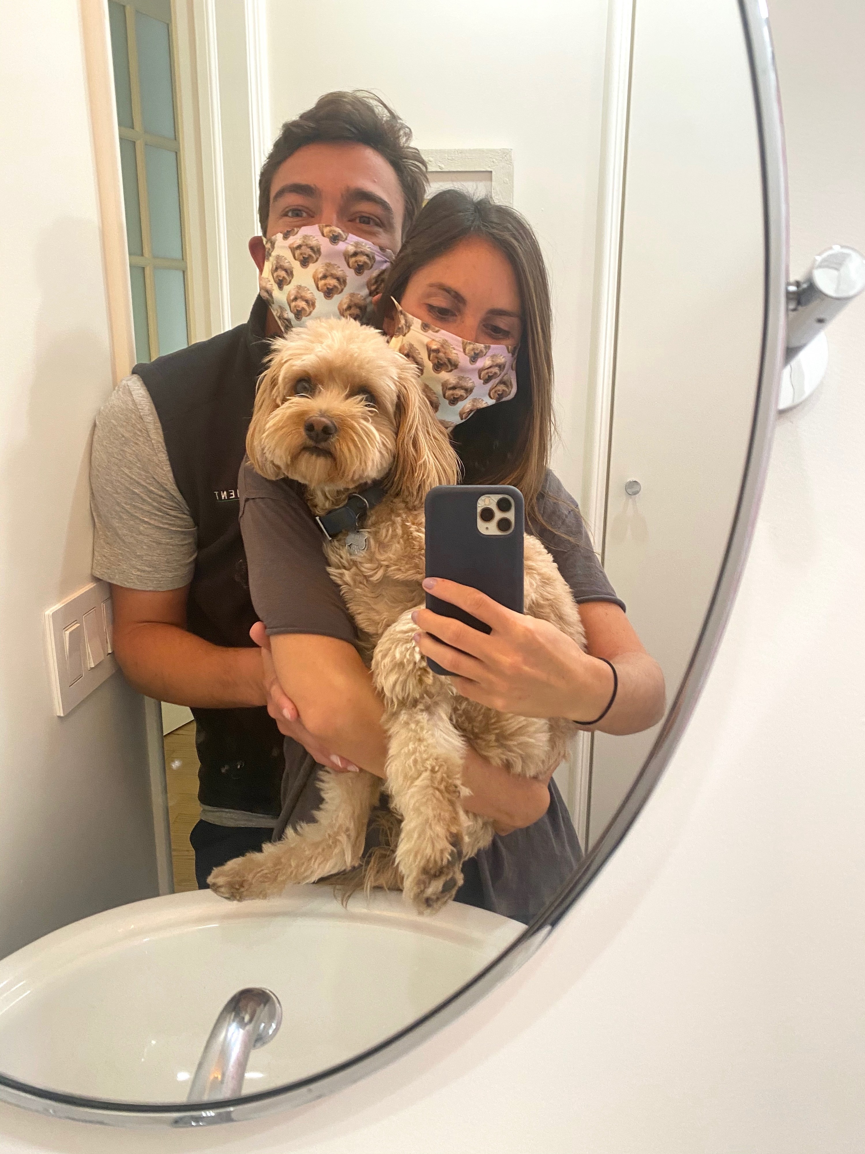 Me, my husband, and our dog posing with our masks in a bathroom mirror.