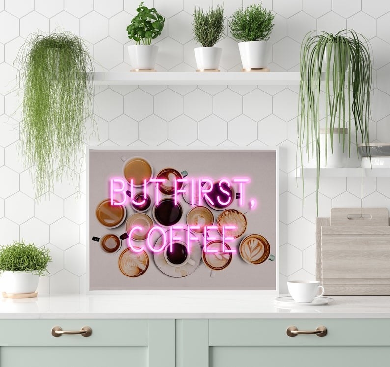 Print of several coffees with and without latte art on white table with word &quot;But First, Coffee in front of them in pink neon lights 