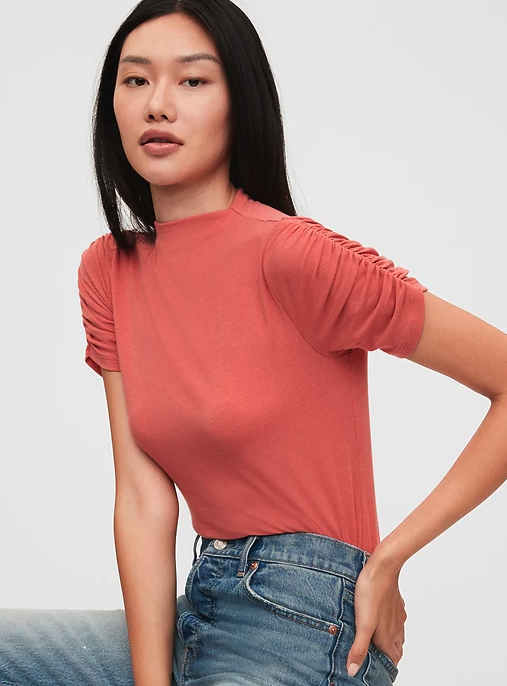 The T-shirt has a high neck and ruched sleeves