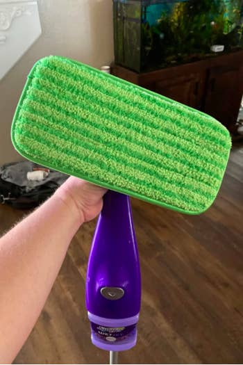 A reviewer holding up their Swiffer with the green pad on the bottom