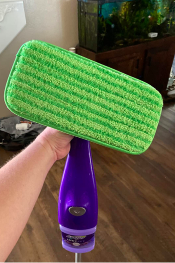 A reviewer holding up their Swiffer with the green pad on the bottom