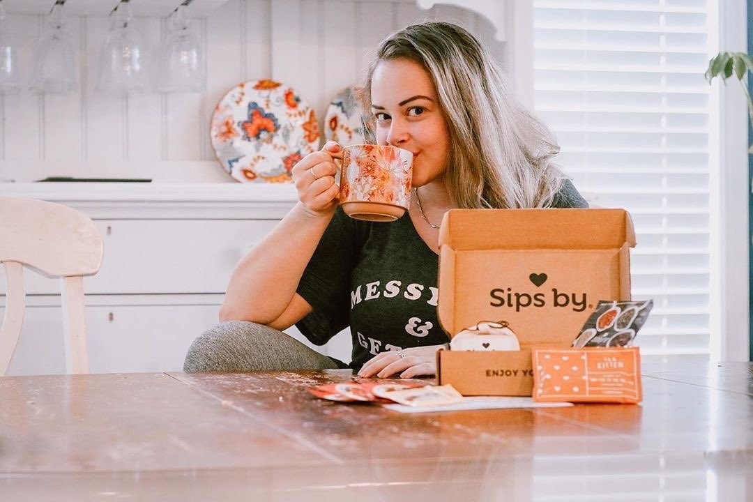 A model drinking tea next to a small box with tea bags in it 