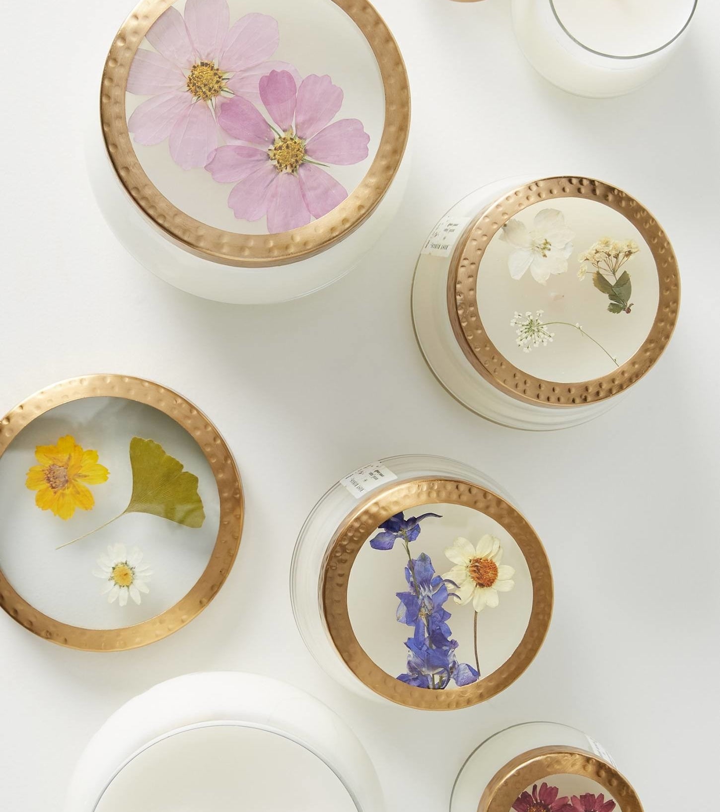 Candles of different sizes with various pressed flowers displayed on the lid