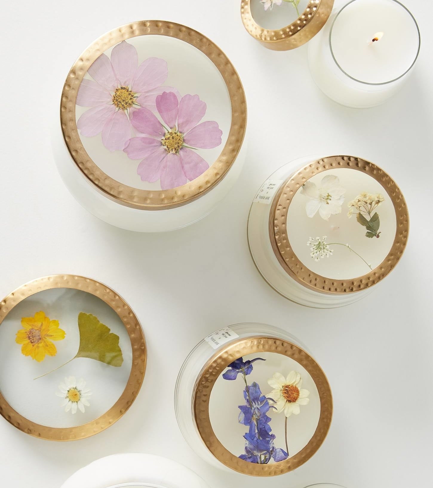 Candles of different sizes with various pressed flowers displayed on the lid