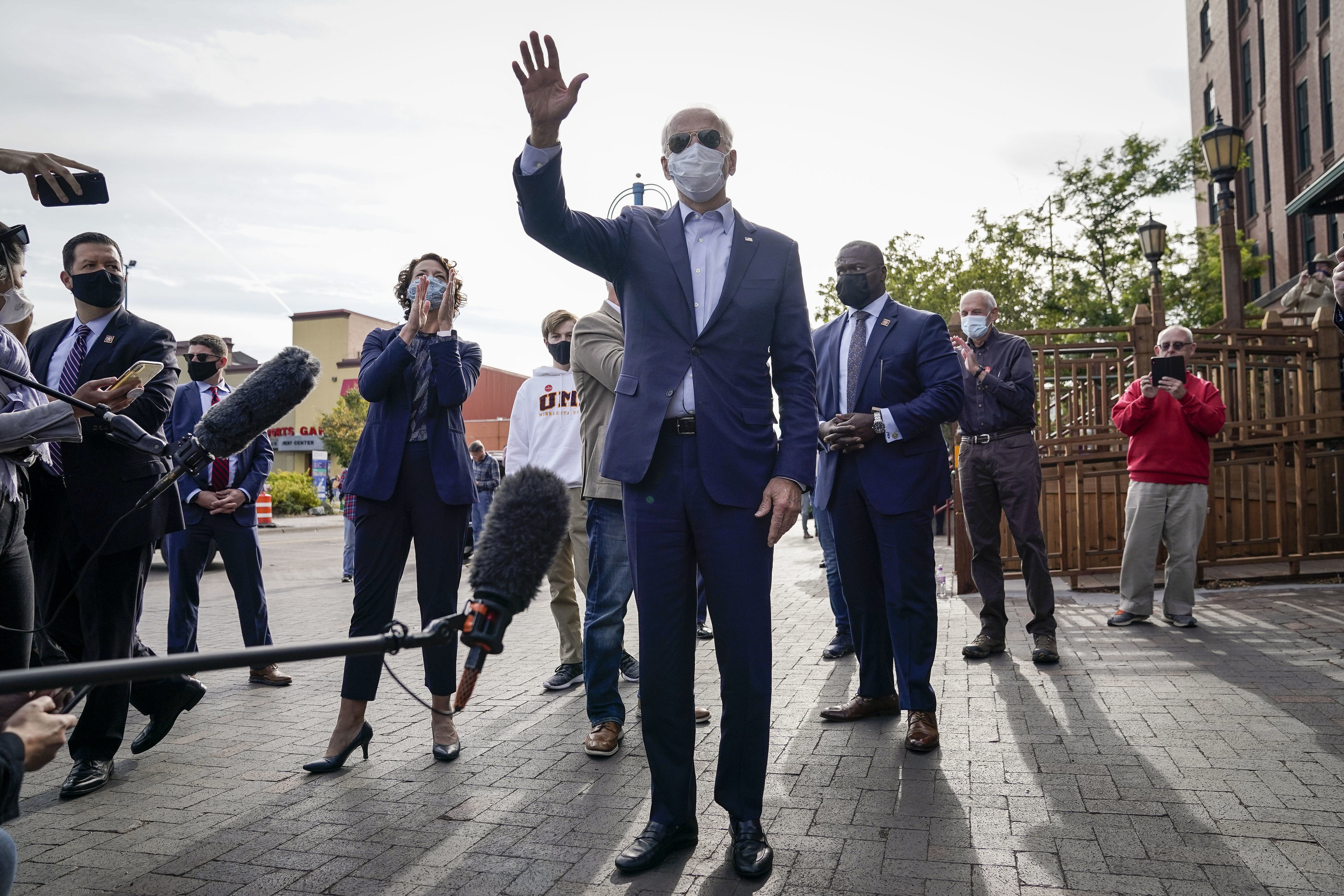 Joe Biden, wearing a face mask and aviator sunglasses, waves in front of reporters