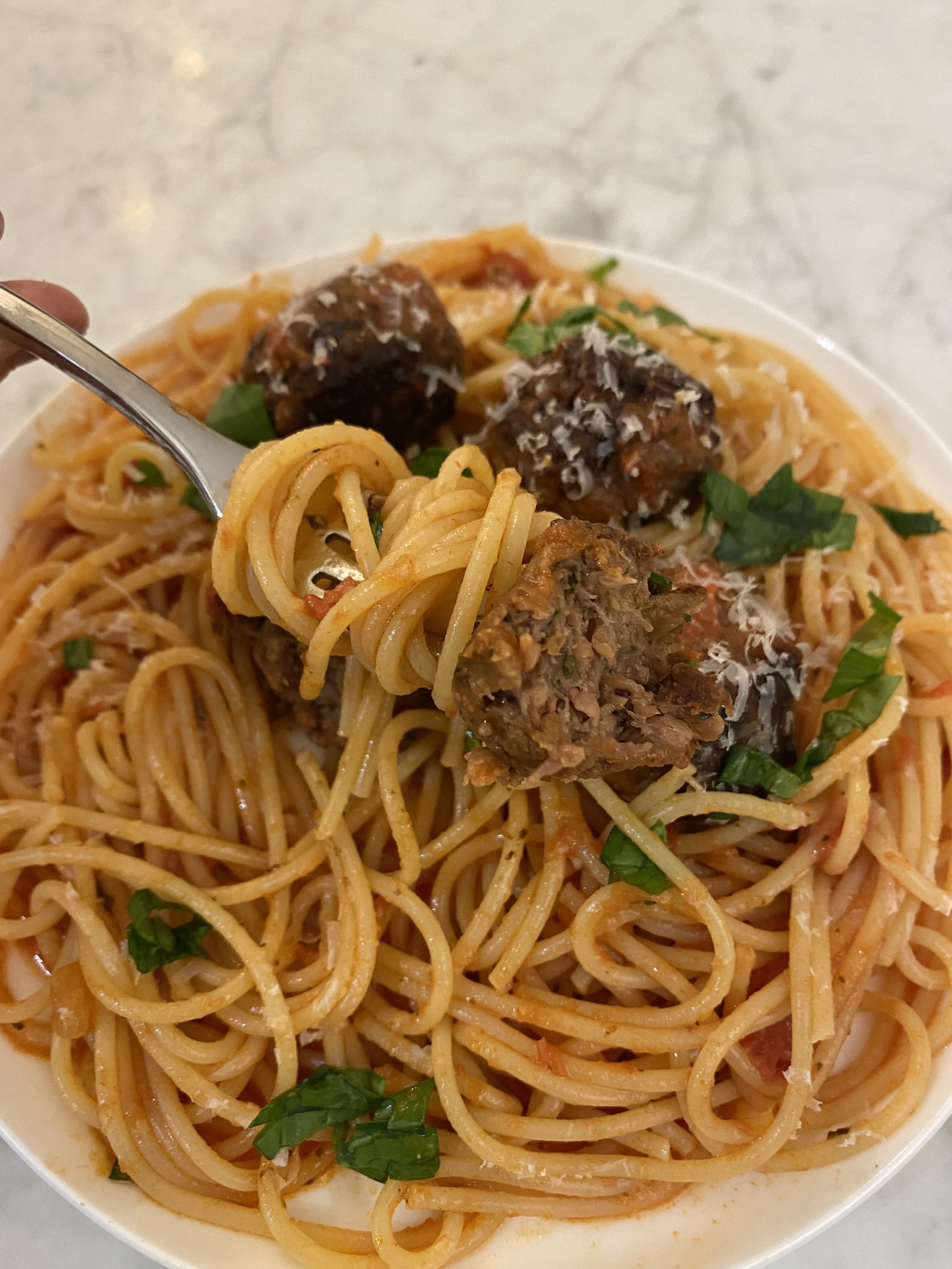 A fork holding swirled spaghetti and a half of a Beyond Meat meatball.