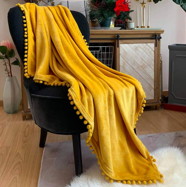 Yellow pompom throw blanket on top of a black velvet armchair in a living room