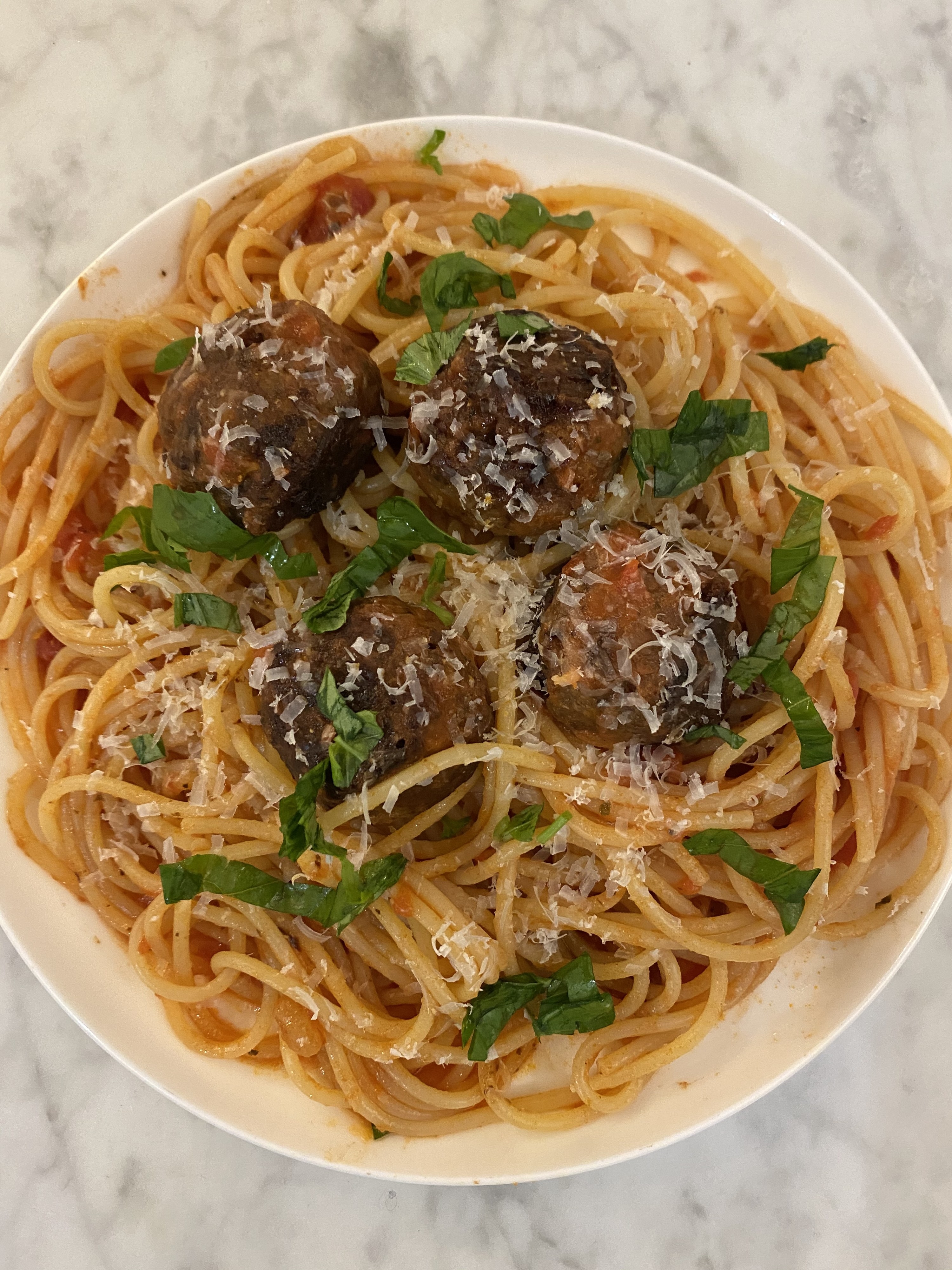 A plate of spaghetti with tomato sauce, basil, parmesan, and Beyond Meat meatballs on top.