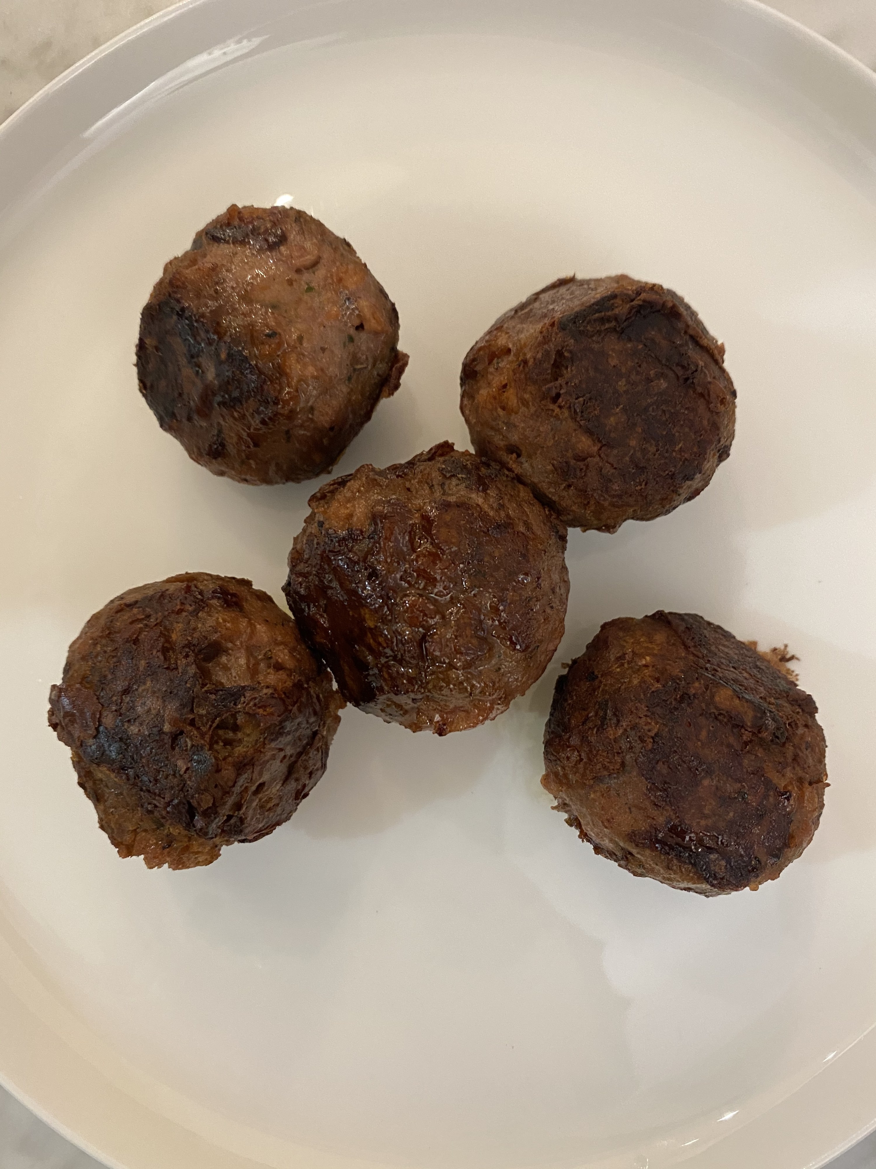 Five cooked Beyond Meat meatballs on a white plate.