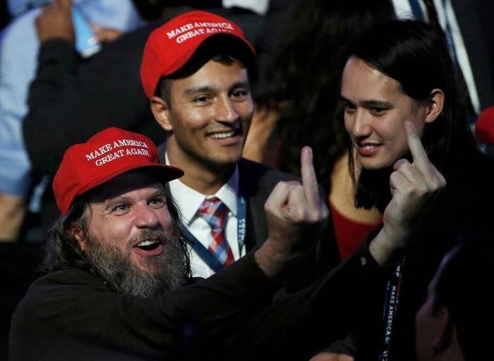 Two men in "Make America Great Again" hats stand next to the CEO of Clearview AI; one of the men in hats holds up two middle fingers