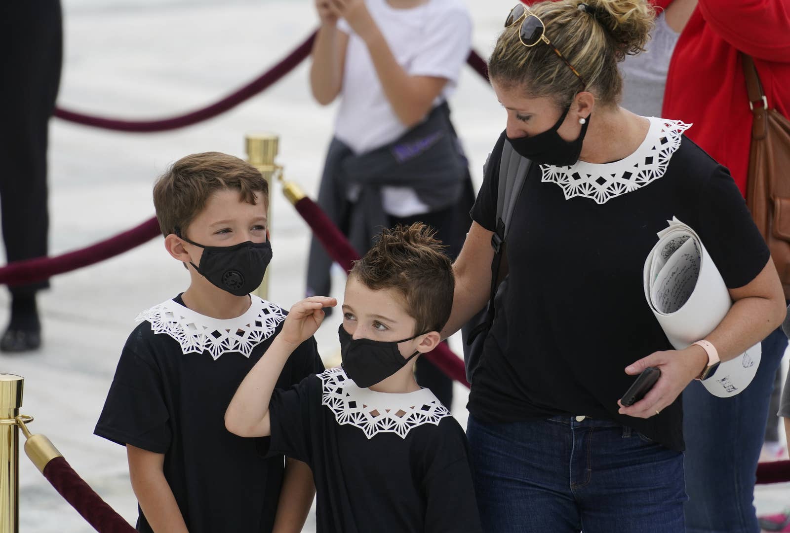 Two boys wearing lace collars salute next to their mom who is also wearing a lace collar
