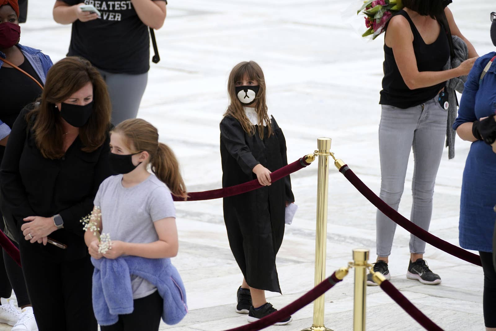 A girl in judges robes with a sad mask stands in line