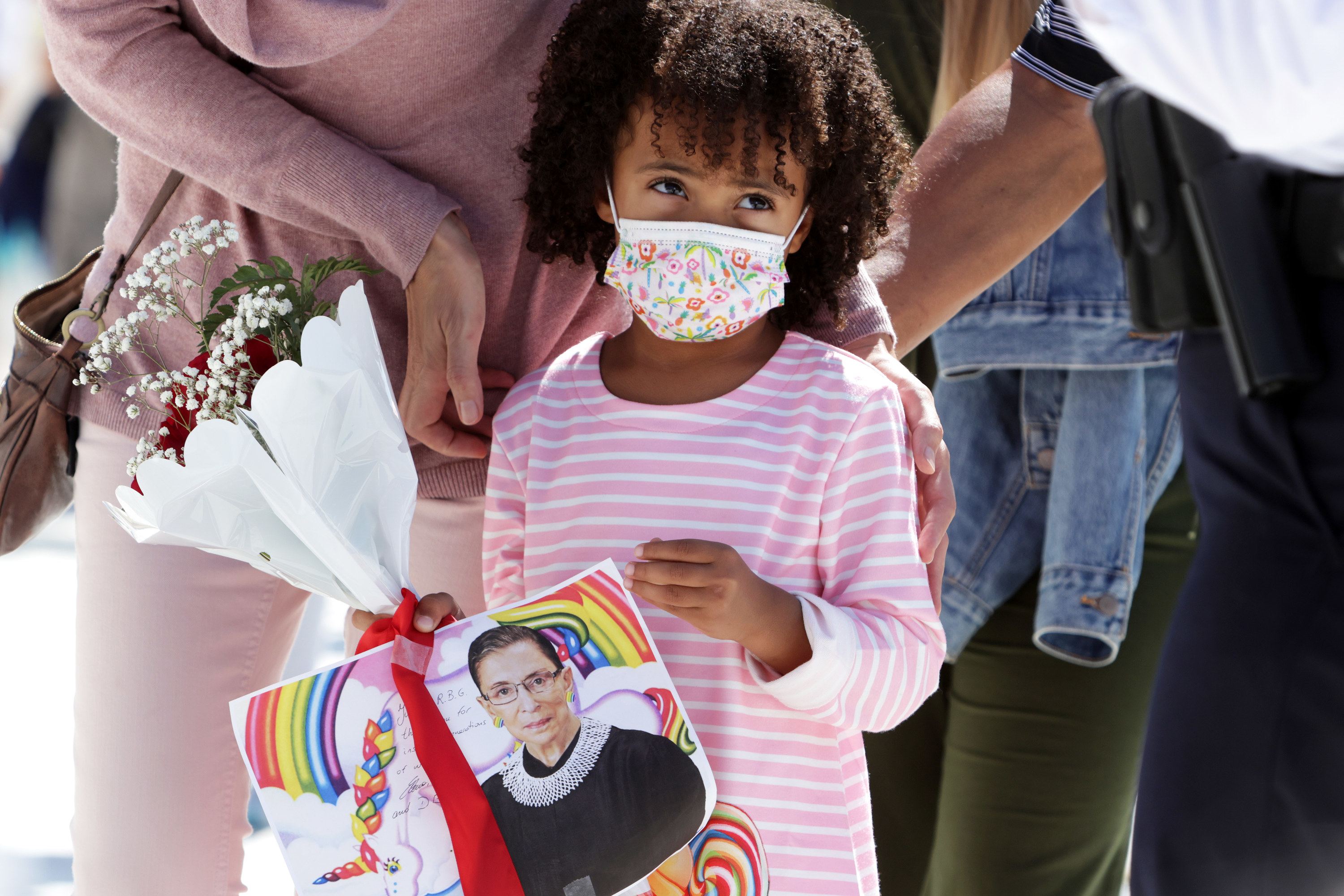 A girl holds flowers and a picture of Ginsburg