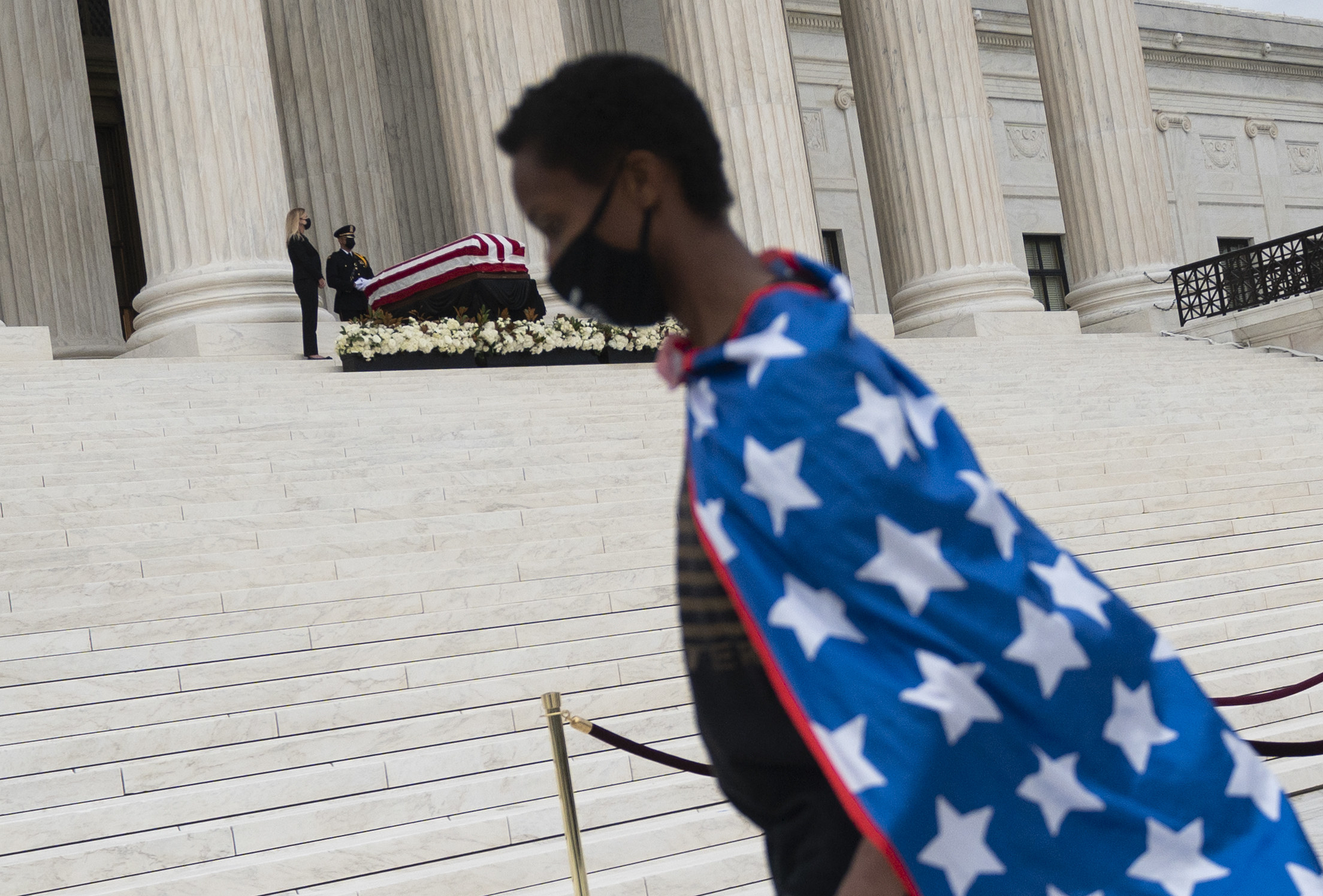 A boy in a flag cape walks in front of where Justice Ginsburg is lying in state