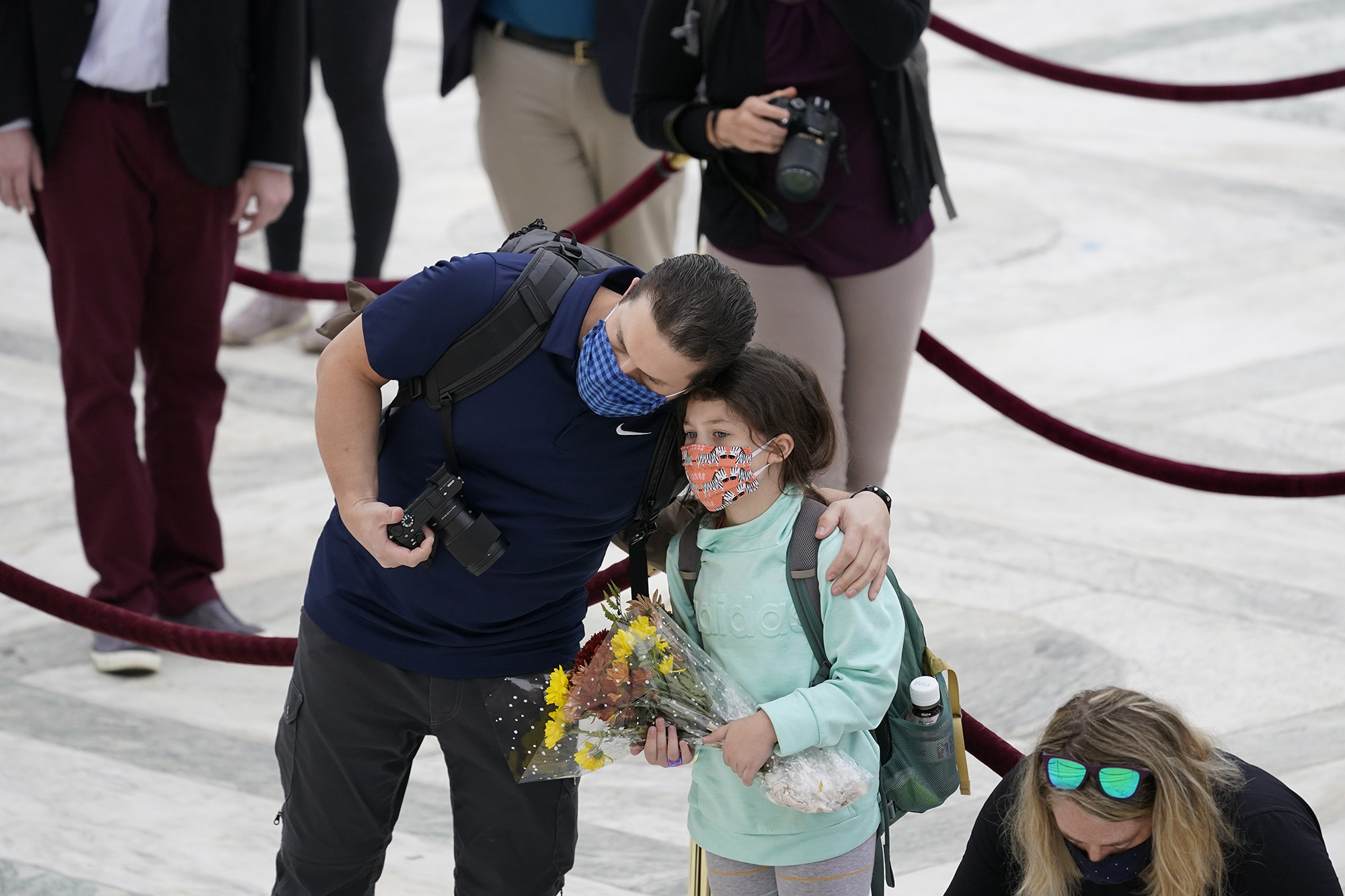 A girl holds flowers while her dad hugs her