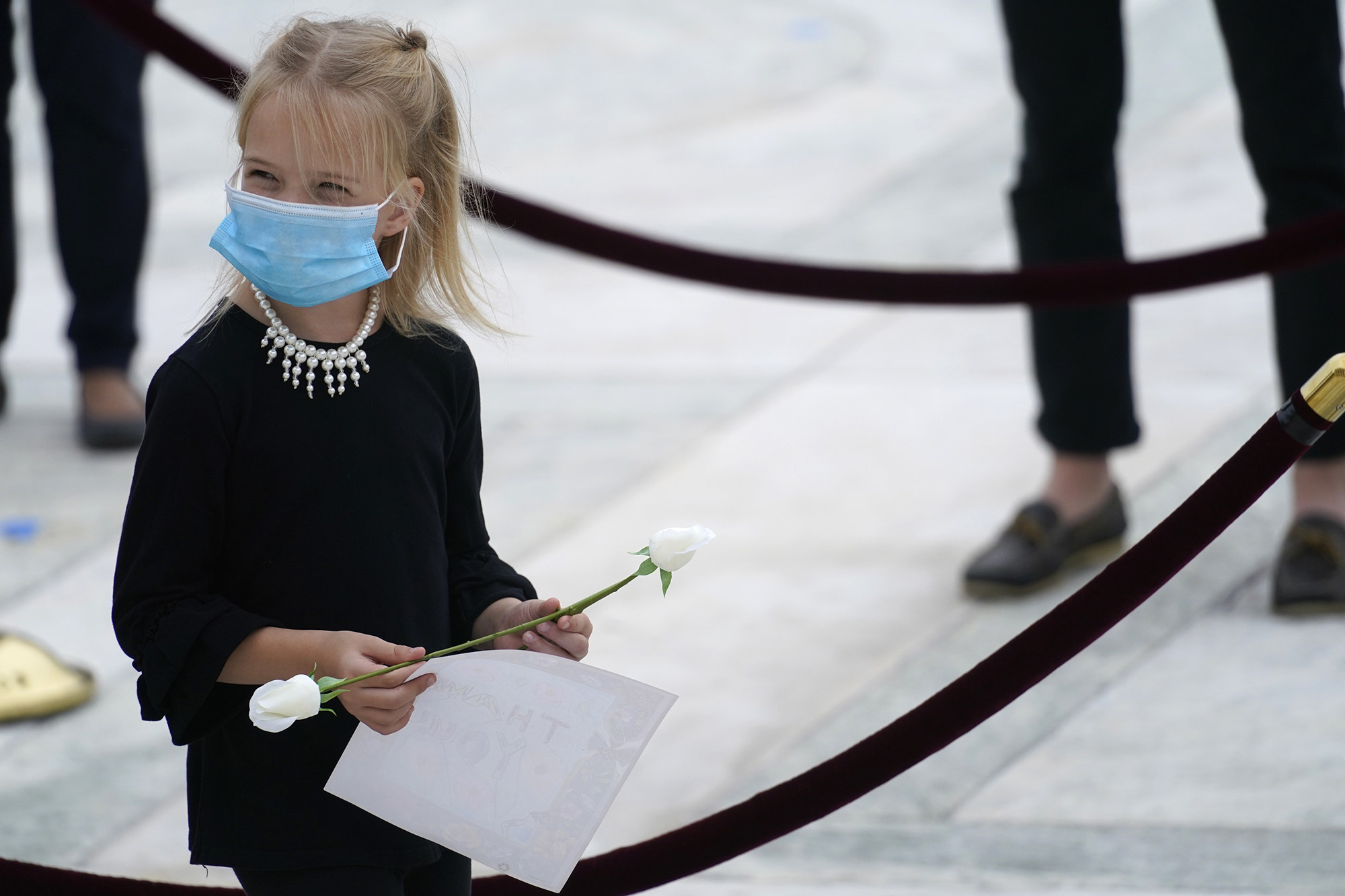 A girl in a face mask and pearls holds a white rose