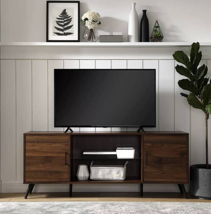 A  dark walnut wood tv console with decor in the center shelves and a TV on top