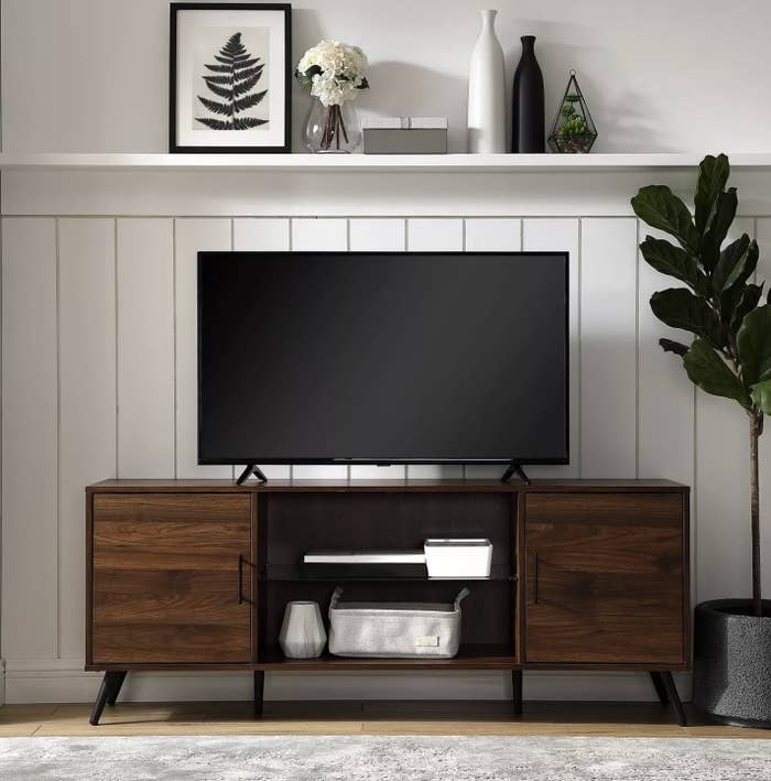 A dark walnut wood tv console with decor in the center shelves and a TV on top