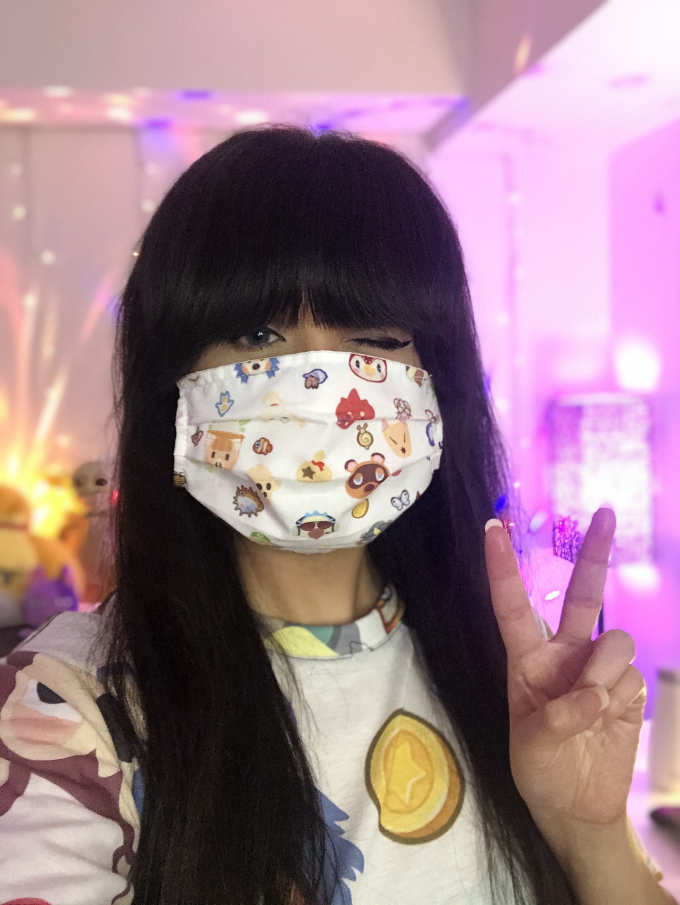 Someone wearing a face mask printed with Animal Crossing and putting up a peace sign