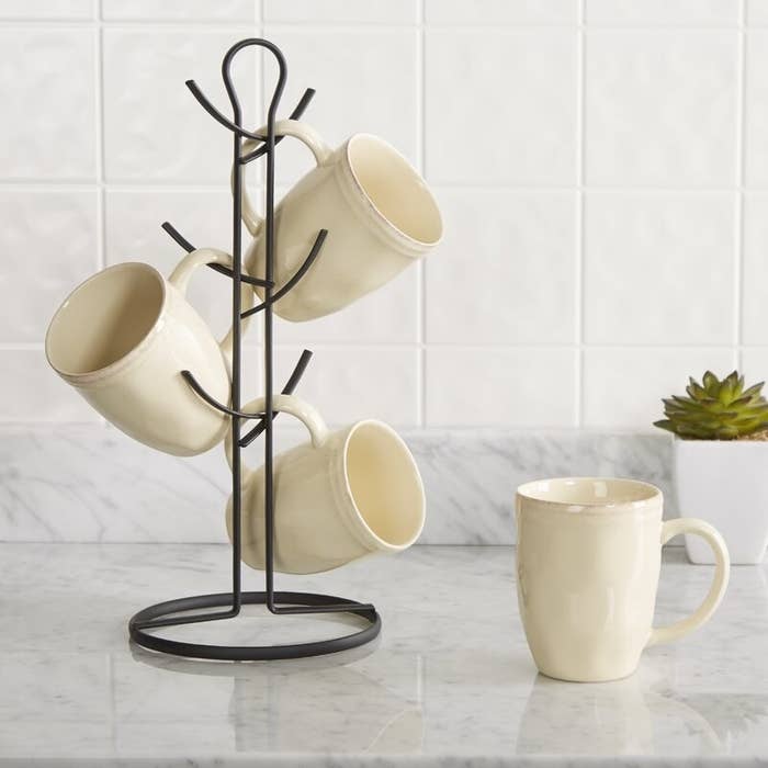 A metal mug tree with six arms that currently holds three mugs on the counter