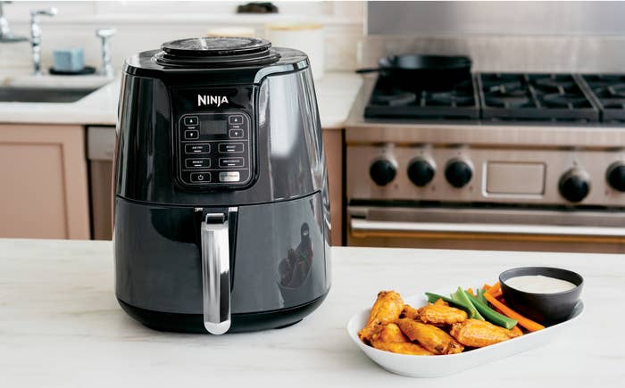 Black ninja air fryer and a plate of buffalo wings on a kitchen counter