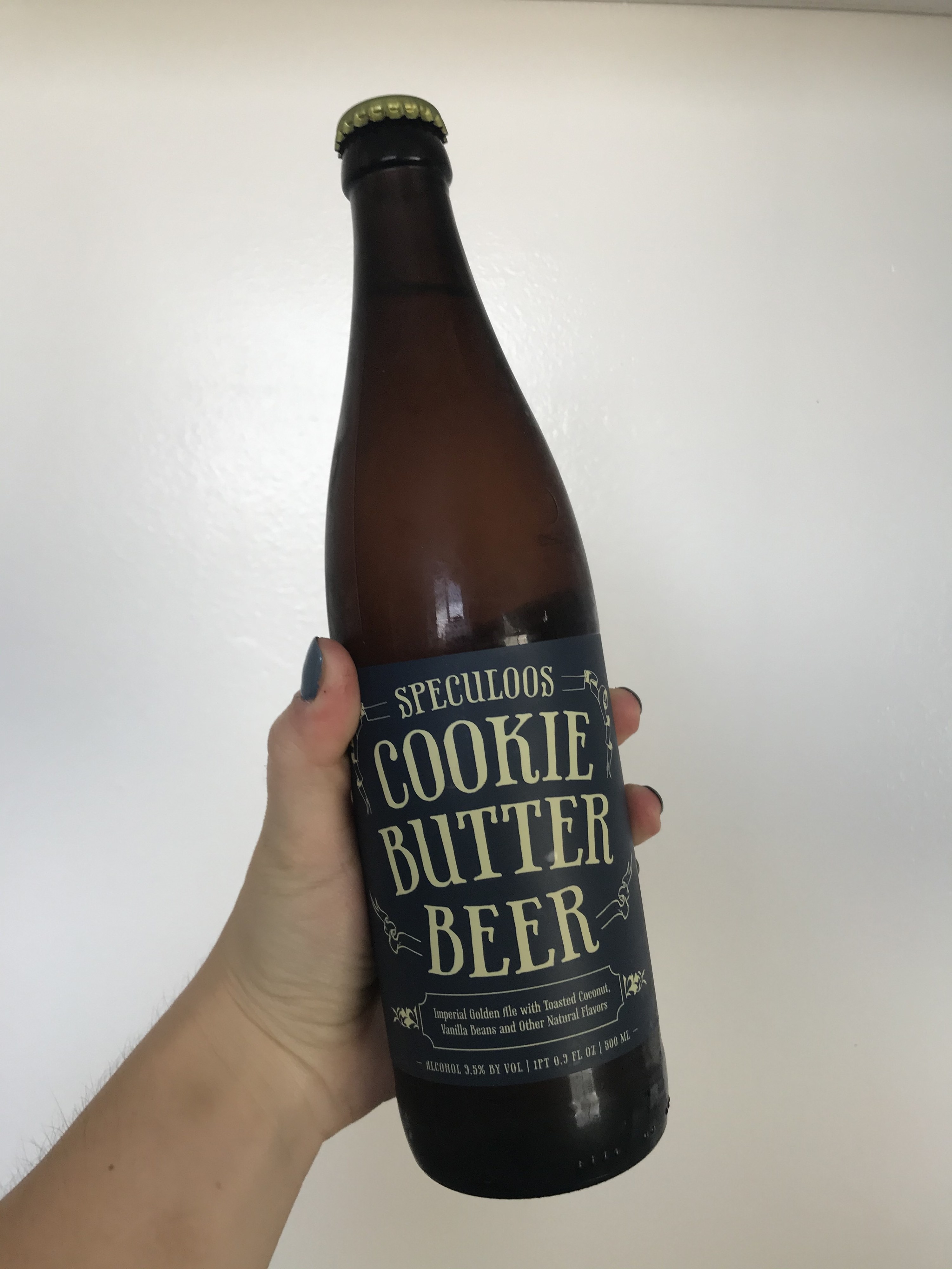 A hand holds up a glass bottle of cookie butter beer against a white backdrop