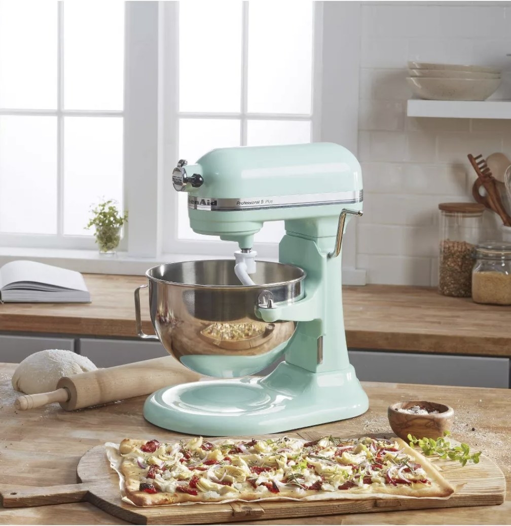 A baby blue Kitchenaid stand mixer next to a flatbread pizza in a kitchen